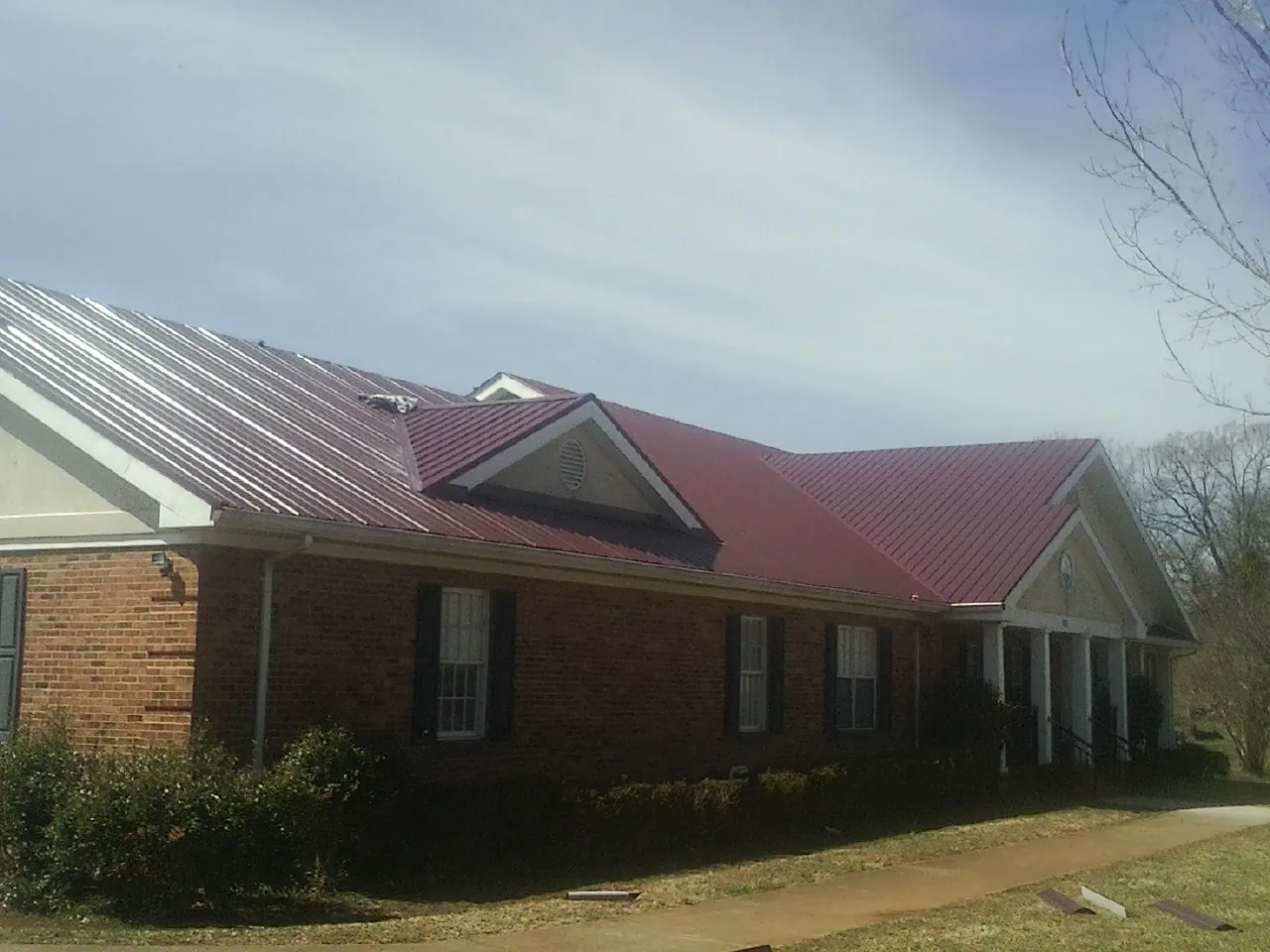 Red metal roof with gabled entries on a long brick building, from a Hail Damage Roof Repair job in Weston